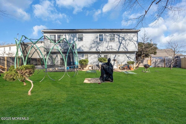 rear view of property featuring a lawn and a trampoline