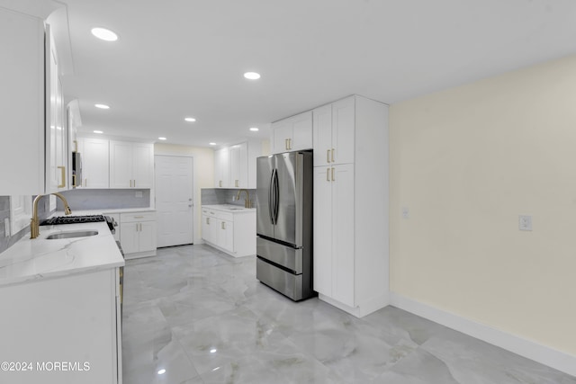 kitchen with sink, stainless steel fridge, white cabinetry, and light stone counters