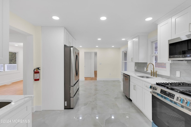 kitchen featuring stainless steel appliances, light stone countertops, sink, white cabinetry, and tasteful backsplash