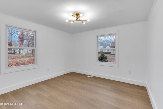 empty room with light wood-type flooring, crown molding, and a chandelier