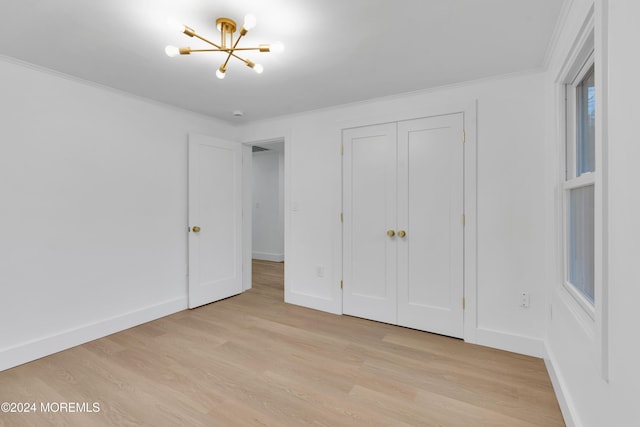 unfurnished bedroom featuring ornamental molding, a closet, a chandelier, and light wood-type flooring