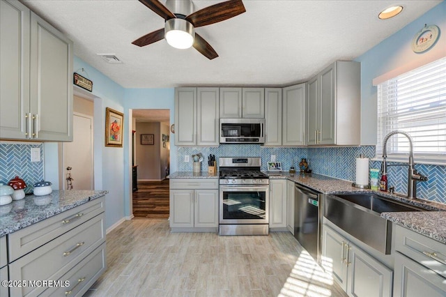 kitchen with stainless steel appliances, light stone counters, decorative backsplash, sink, and light hardwood / wood-style flooring