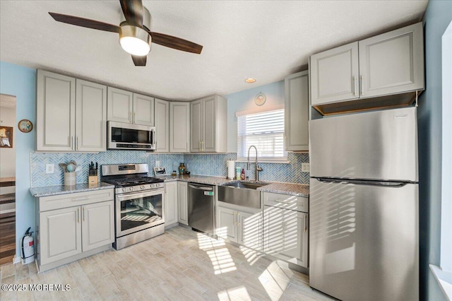 kitchen with stainless steel appliances, sink, ceiling fan, light hardwood / wood-style floors, and light stone countertops