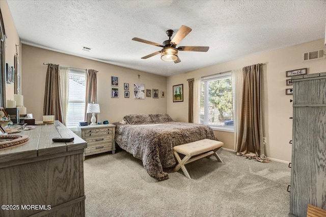 bedroom with ceiling fan, light colored carpet, and a textured ceiling