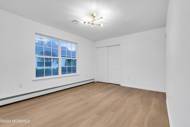 unfurnished bedroom featuring a closet, a chandelier, baseboard heating, and light hardwood / wood-style floors