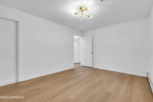 empty room featuring light hardwood / wood-style floors, an inviting chandelier, and a baseboard radiator