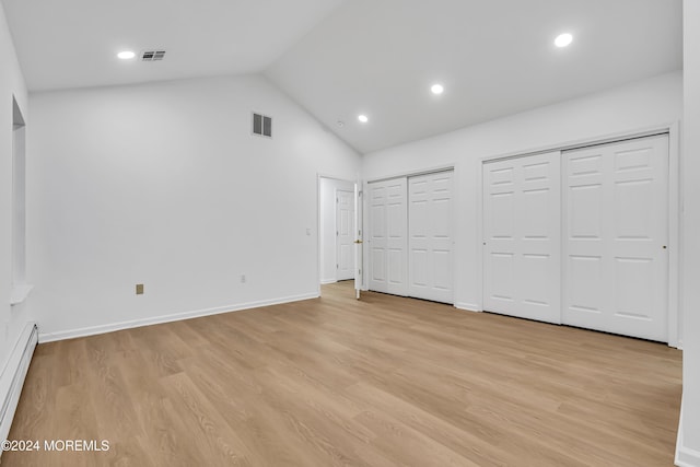 unfurnished bedroom featuring vaulted ceiling, a baseboard radiator, light hardwood / wood-style floors, and multiple closets