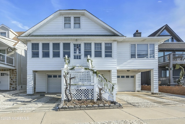 raised beach house with driveway, a chimney, and an attached garage