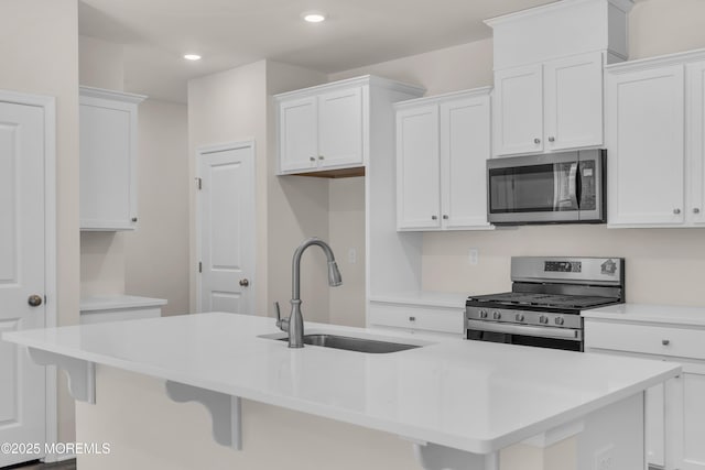 kitchen with a kitchen breakfast bar, appliances with stainless steel finishes, sink, white cabinetry, and a kitchen island with sink