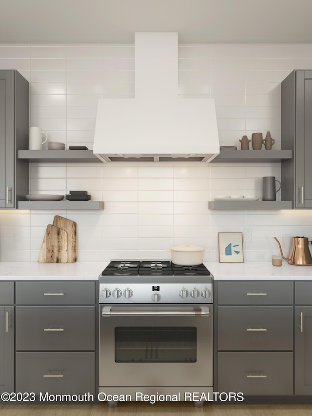 kitchen with gas range, range hood, gray cabinetry, and decorative backsplash