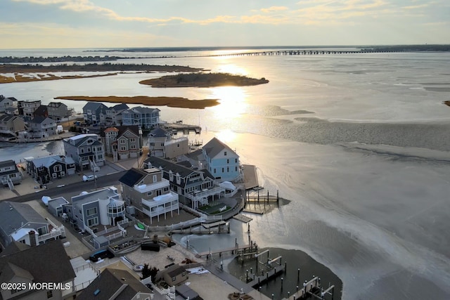 aerial view at dusk featuring a water view and a beach view