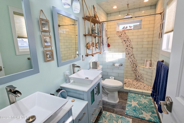 bathroom with toilet, a tile shower, and vanity