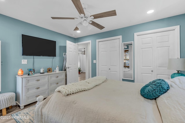 bedroom with ceiling fan, multiple closets, and wood-type flooring