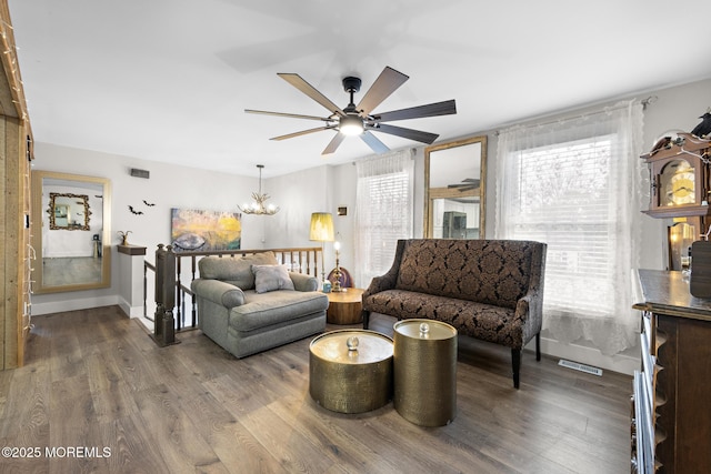 living room with ceiling fan with notable chandelier and dark hardwood / wood-style floors