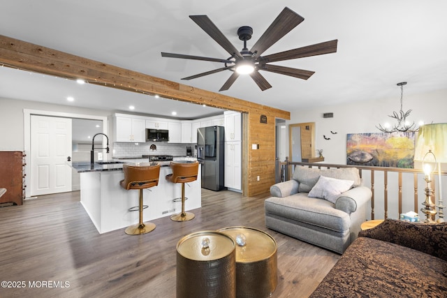 living room featuring sink, ceiling fan with notable chandelier, beamed ceiling, and dark hardwood / wood-style floors