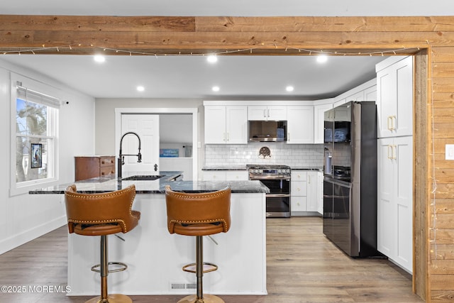 kitchen with stainless steel appliances, a kitchen island with sink, backsplash, white cabinetry, and a kitchen breakfast bar