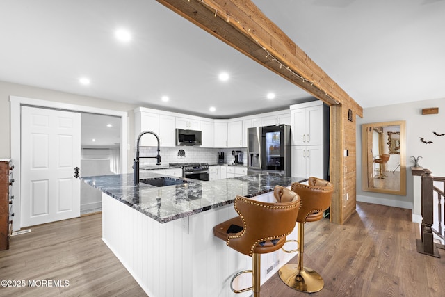 kitchen featuring stainless steel appliances, decorative backsplash, white cabinetry, dark stone countertops, and sink