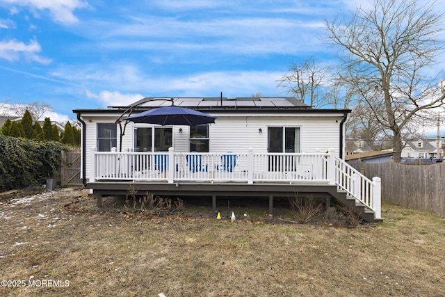 rear view of house featuring solar panels, a deck, and a lawn