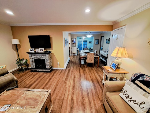 living room featuring ceiling fan, a stone fireplace, ornamental molding, and hardwood / wood-style flooring