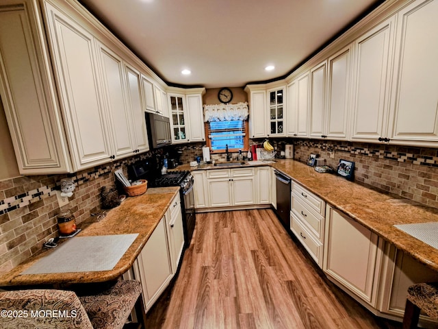 kitchen with light hardwood / wood-style floors, black appliances, decorative backsplash, sink, and light stone countertops