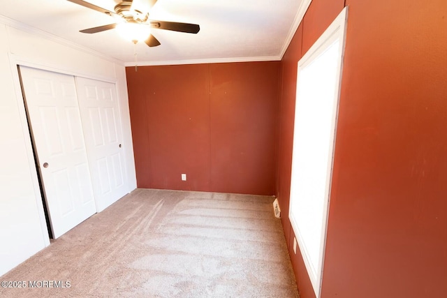 unfurnished bedroom featuring ornamental molding, light colored carpet, ceiling fan, and a closet