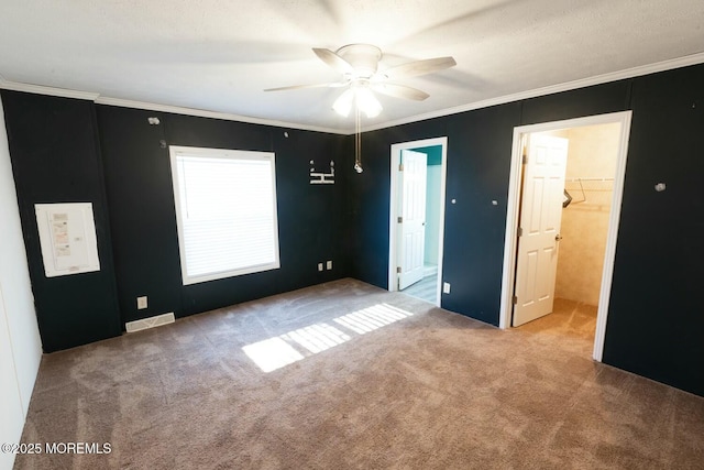 unfurnished bedroom with a walk in closet, ceiling fan, ornamental molding, and light colored carpet