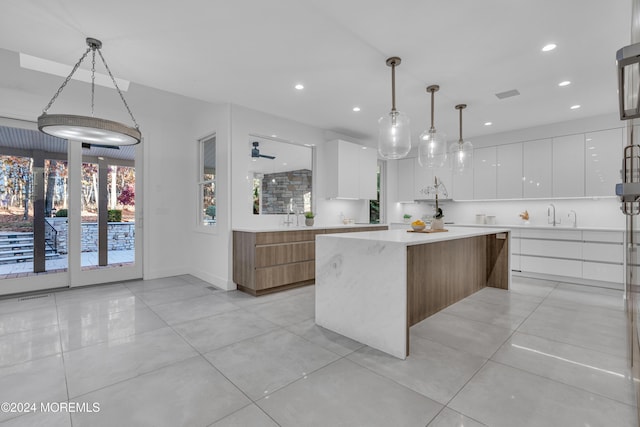 kitchen featuring pendant lighting, a spacious island, light tile patterned floors, white cabinetry, and sink