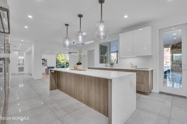 kitchen with light stone counters, hanging light fixtures, a large island, white cabinets, and sink