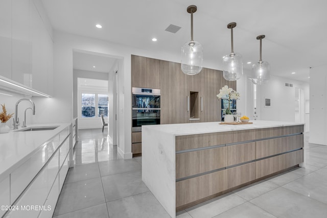 kitchen featuring double oven, sink, hanging light fixtures, and white cabinetry