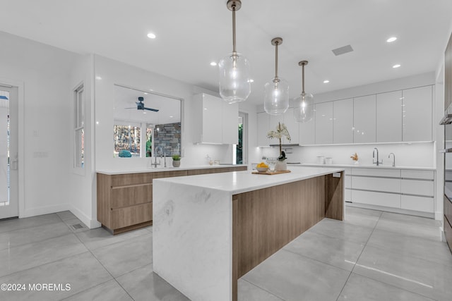 kitchen with hanging light fixtures, a center island, white cabinets, ceiling fan, and sink