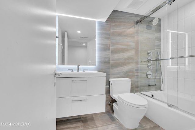 full bathroom featuring combined bath / shower with glass door, tile walls, vanity, and toilet