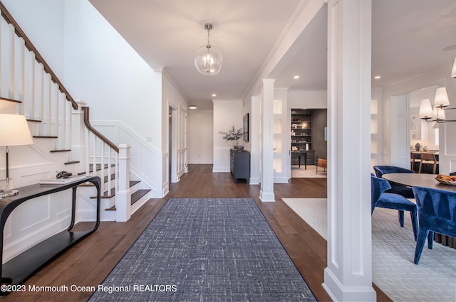 entrance foyer featuring ornate columns, an inviting chandelier, ornamental molding, and dark wood-type flooring