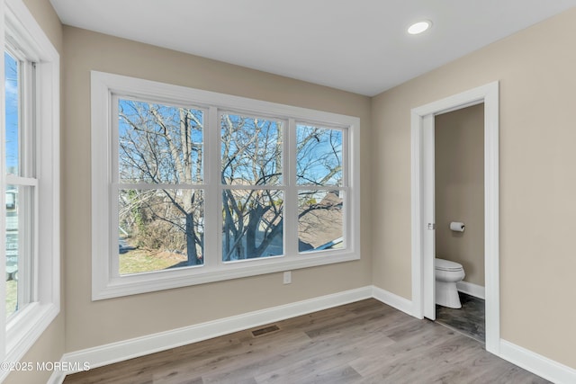 interior space with multiple windows, wood-type flooring, and connected bathroom