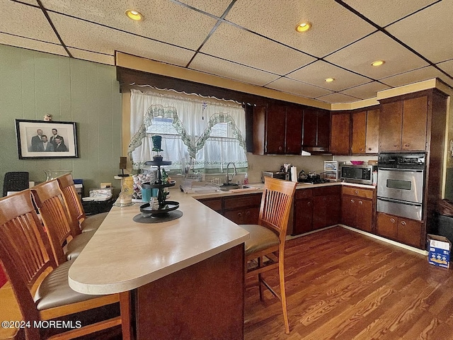 kitchen featuring sink, oven, kitchen peninsula, wood-type flooring, and dark brown cabinetry