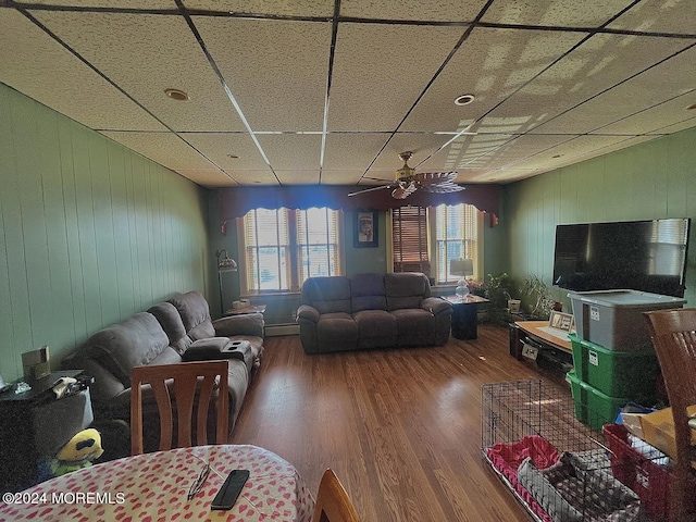 living room with ceiling fan, a drop ceiling, a baseboard heating unit, and wood-type flooring