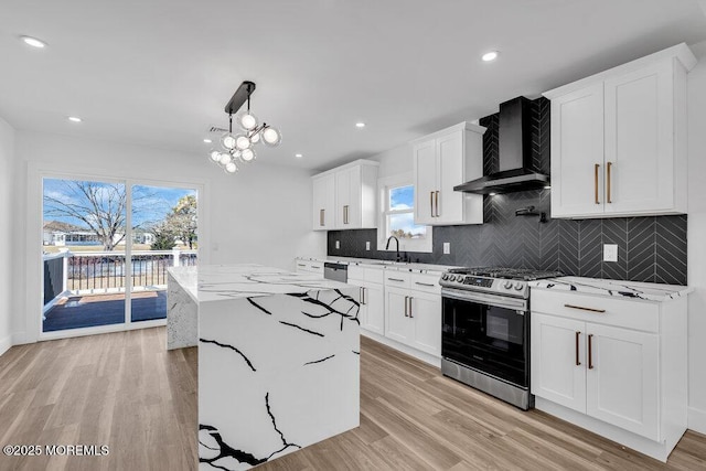 kitchen featuring wall chimney exhaust hood, gas stove, white cabinets, and hanging light fixtures