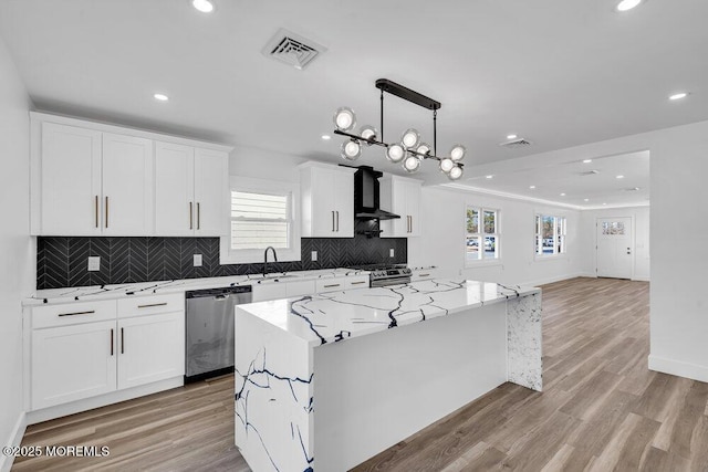 kitchen with appliances with stainless steel finishes, a center island, wall chimney exhaust hood, white cabinetry, and light stone counters