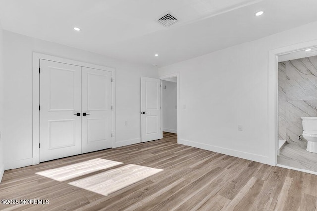 unfurnished bedroom with ensuite bathroom, light wood-type flooring, and a closet