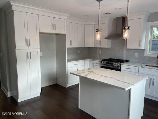 kitchen with wall chimney exhaust hood, stainless steel gas range oven, white cabinetry, hanging light fixtures, and a kitchen island