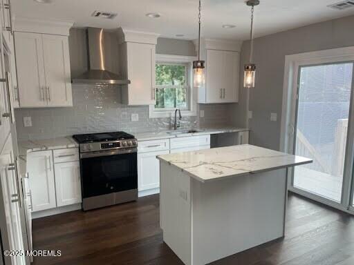 kitchen with wall chimney range hood, sink, stainless steel gas range oven, white cabinets, and a kitchen island