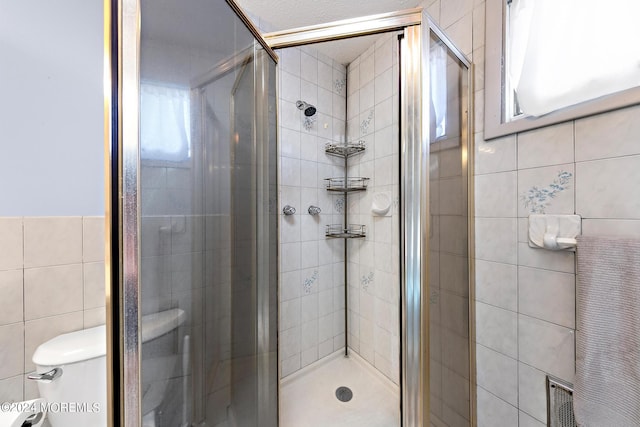 bathroom with tile walls, a shower with door, and toilet