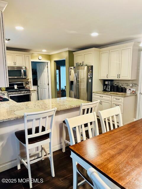 kitchen featuring light stone countertops, appliances with stainless steel finishes, dark hardwood / wood-style flooring, backsplash, and a breakfast bar