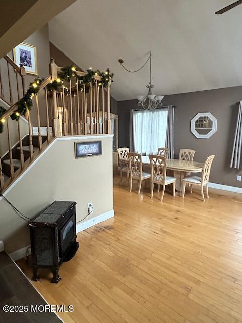 dining room featuring a wood stove, hardwood / wood-style floors, a notable chandelier, and vaulted ceiling