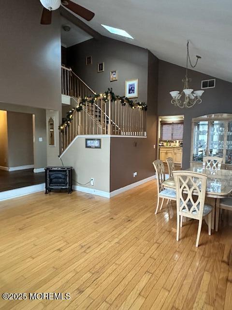 unfurnished dining area featuring high vaulted ceiling, a skylight, ceiling fan with notable chandelier, and light hardwood / wood-style floors