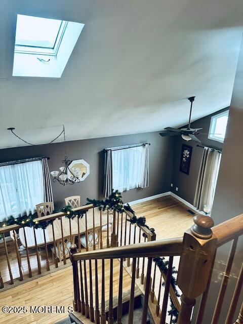 staircase with lofted ceiling with skylight, ceiling fan with notable chandelier, and hardwood / wood-style floors