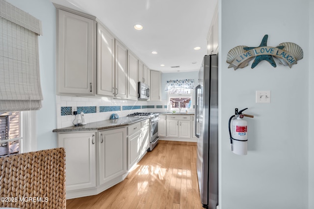 kitchen with stainless steel appliances, dark stone counters, white cabinets, light hardwood / wood-style flooring, and backsplash