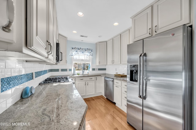 kitchen featuring light wood-type flooring, tasteful backsplash, light stone counters, and appliances with stainless steel finishes