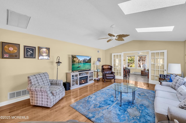 living room featuring a textured ceiling, french doors, lofted ceiling with skylight, hardwood / wood-style floors, and ceiling fan