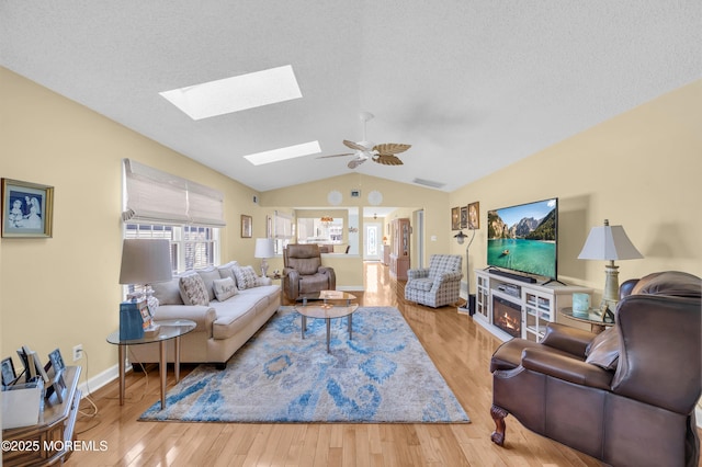 living room with a textured ceiling, ceiling fan, vaulted ceiling, and light hardwood / wood-style flooring