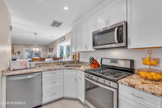 kitchen with white cabinets, stainless steel appliances, sink, a notable chandelier, and light stone counters